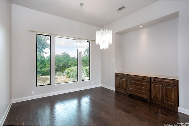 spare room featuring a wealth of natural light, dark hardwood / wood-style floors, and a chandelier