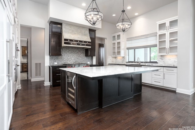 kitchen with premium range hood, white cabinets, dark wood-type flooring, light stone countertops, and a kitchen island