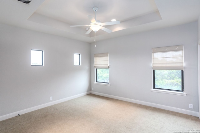 carpeted spare room featuring ceiling fan, a healthy amount of sunlight, and a tray ceiling