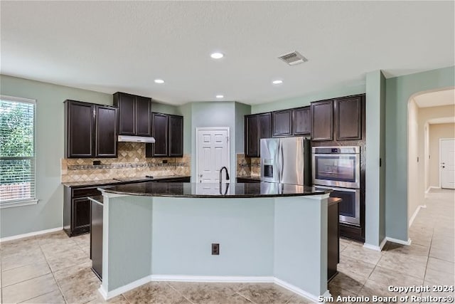 kitchen with backsplash, sink, a kitchen island with sink, appliances with stainless steel finishes, and dark brown cabinets