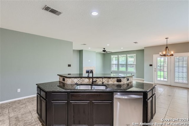 kitchen with dishwasher, decorative light fixtures, dark stone countertops, sink, and a kitchen island with sink