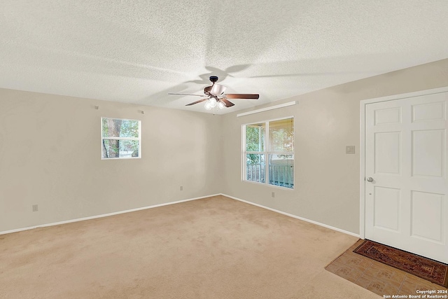 empty room with a textured ceiling, plenty of natural light, ceiling fan, and light carpet