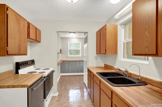 kitchen featuring a textured ceiling, electric range, white fridge, and sink