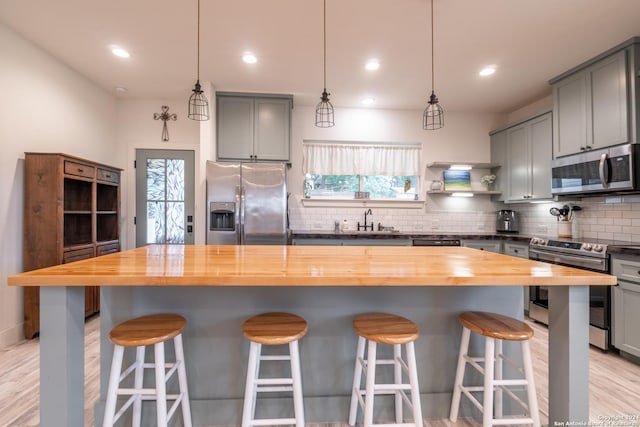 kitchen with pendant lighting, wood counters, a center island, appliances with stainless steel finishes, and tasteful backsplash