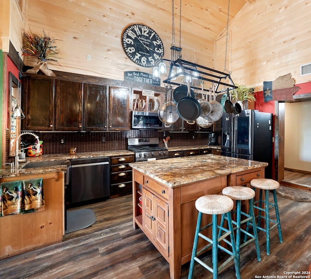 kitchen with appliances with stainless steel finishes, sink, dark hardwood / wood-style flooring, a center island, and light stone countertops