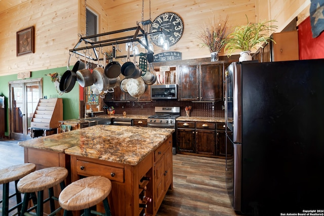 kitchen featuring light stone counters, a center island, high vaulted ceiling, dark hardwood / wood-style flooring, and stainless steel appliances