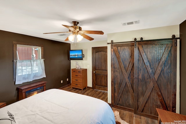 bedroom with ceiling fan, wood-type flooring, and a barn door