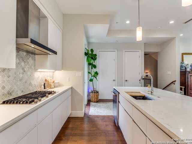 kitchen with light stone counters, stainless steel appliances, wall chimney range hood, decorative light fixtures, and white cabinets