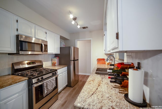 kitchen with sink, stainless steel appliances, light stone counters, light hardwood / wood-style floors, and white cabinets