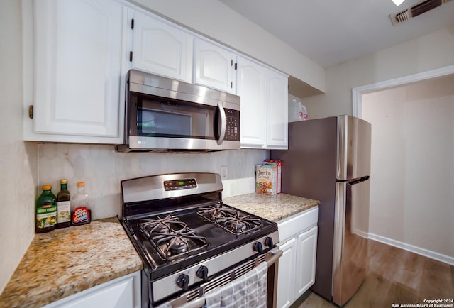 kitchen with white cabinets, tasteful backsplash, light stone counters, wood-type flooring, and stainless steel appliances