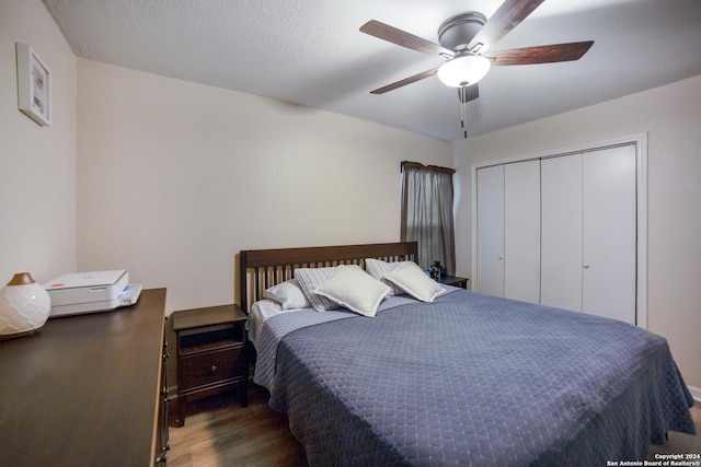 bedroom with a textured ceiling, ceiling fan, dark wood-type flooring, and a closet