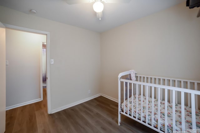 bedroom featuring a crib, dark hardwood / wood-style flooring, and ceiling fan