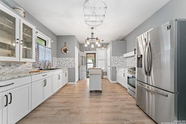 kitchen with appliances with stainless steel finishes, light wood-type flooring, light stone counters, white cabinetry, and hanging light fixtures