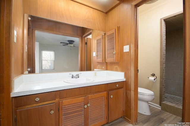 bathroom with ceiling fan, wood-type flooring, tiled shower, toilet, and vanity