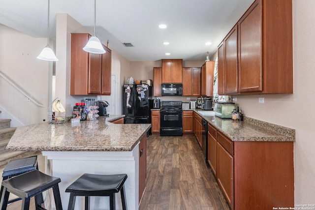 kitchen with black appliances, dark hardwood / wood-style flooring, hanging light fixtures, kitchen peninsula, and a breakfast bar area