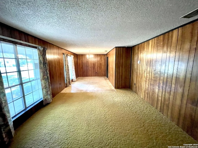 carpeted empty room featuring a chandelier, wooden walls, and a textured ceiling