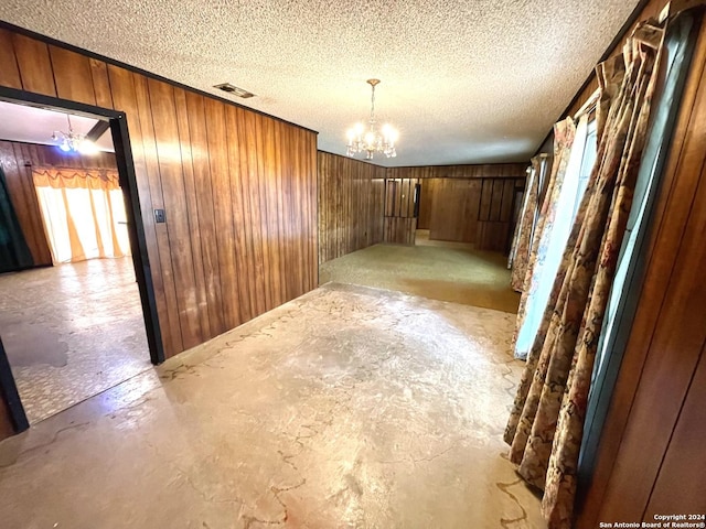 empty room with an inviting chandelier, wooden walls, and a textured ceiling