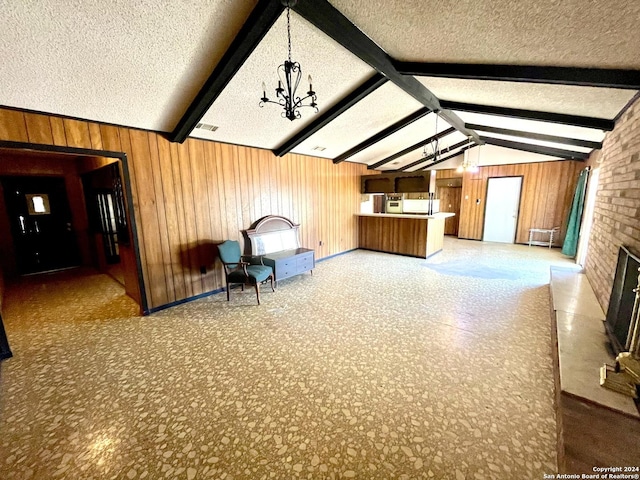 unfurnished room featuring a textured ceiling, wood walls, a notable chandelier, and lofted ceiling with beams