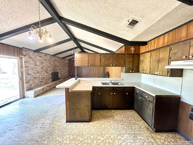 kitchen with kitchen peninsula, sink, lofted ceiling with beams, a textured ceiling, and pendant lighting