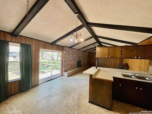 kitchen featuring lofted ceiling with beams, a textured ceiling, decorative light fixtures, a fireplace, and wooden walls