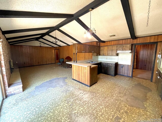 kitchen with hanging light fixtures, a textured ceiling, lofted ceiling with beams, wood walls, and sink