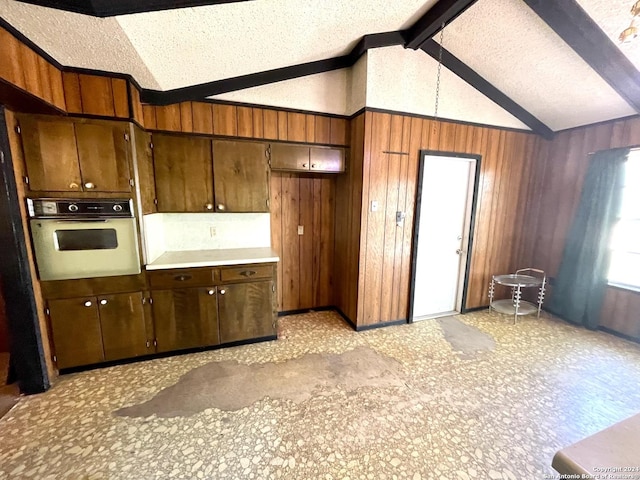 kitchen featuring wooden walls, a textured ceiling, oven, and vaulted ceiling with beams