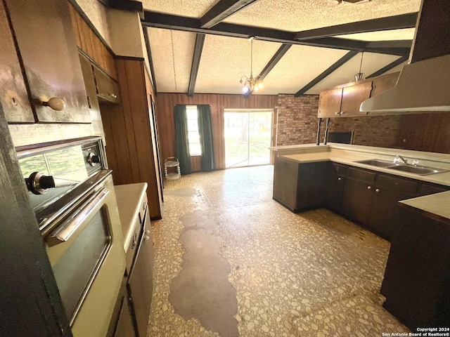 kitchen featuring sink, vaulted ceiling with beams, pendant lighting, wood walls, and white oven