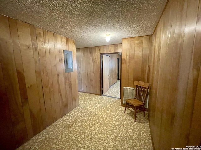 hall with electric panel, wood walls, and a textured ceiling