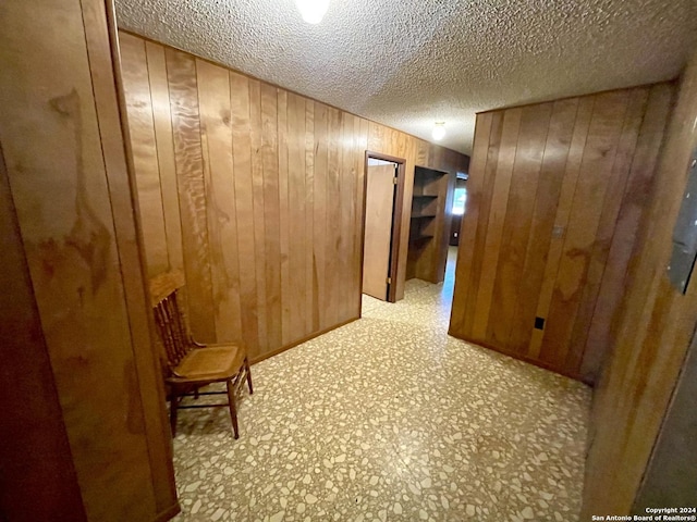 hallway featuring a textured ceiling and wooden walls