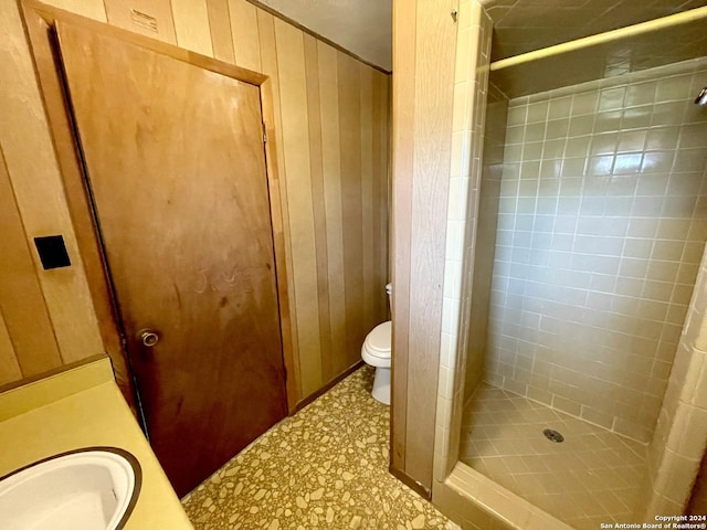 bathroom with vanity, tiled shower, toilet, and wooden walls