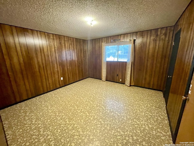 unfurnished room featuring wood walls and a textured ceiling