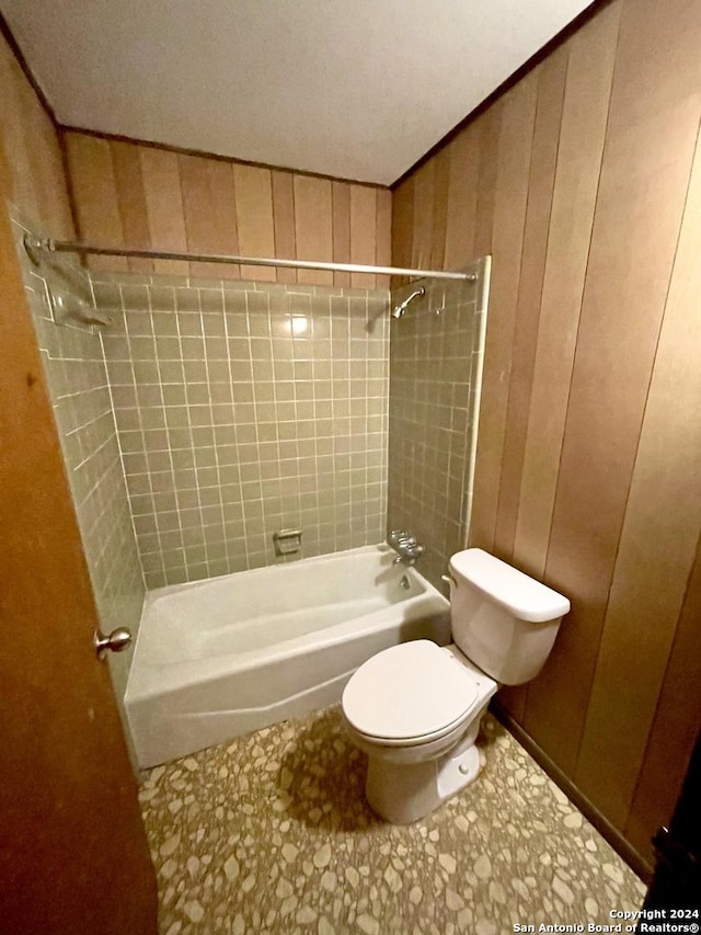 bathroom with wood walls, tiled shower / bath combo, and toilet