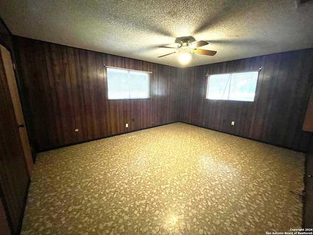 unfurnished room with ceiling fan, wood walls, and a textured ceiling