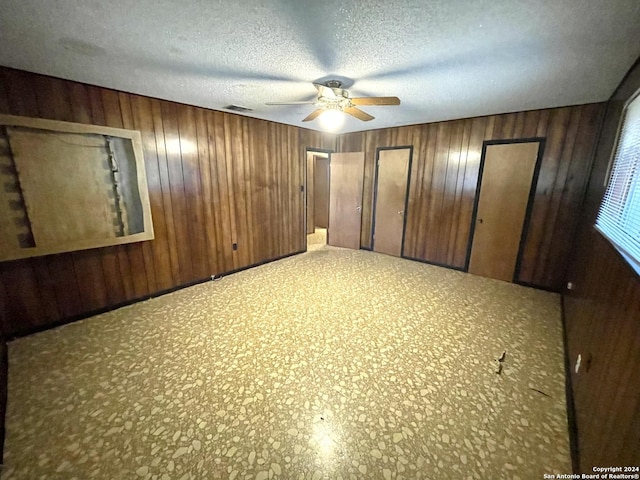 unfurnished bedroom featuring ceiling fan, wood walls, and a textured ceiling