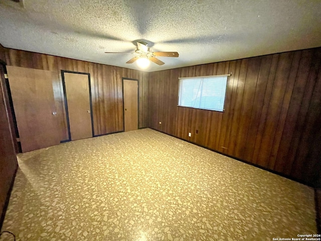 unfurnished bedroom featuring ceiling fan, wooden walls, a textured ceiling, and two closets