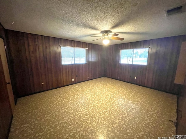 unfurnished room with ceiling fan, wood walls, and a textured ceiling