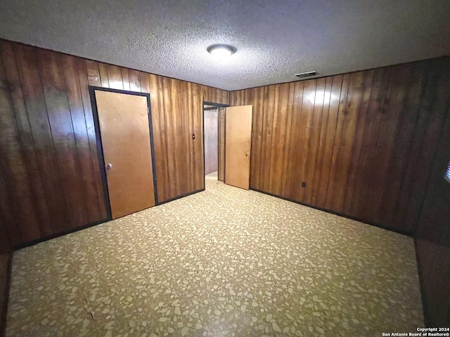 unfurnished bedroom with a textured ceiling and wooden walls