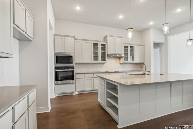 kitchen featuring built in microwave, sink, pendant lighting, oven, and a kitchen island with sink