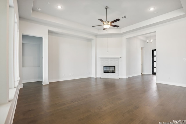 unfurnished living room with dark wood-type flooring, a fireplace, a raised ceiling, and ceiling fan