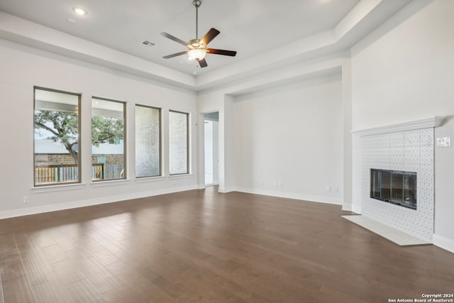 unfurnished living room with a tiled fireplace, dark hardwood / wood-style flooring, a raised ceiling, and ceiling fan