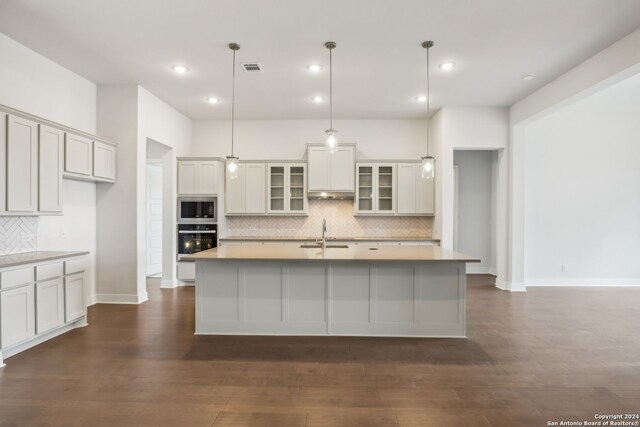 kitchen featuring built in microwave, decorative light fixtures, oven, and an island with sink