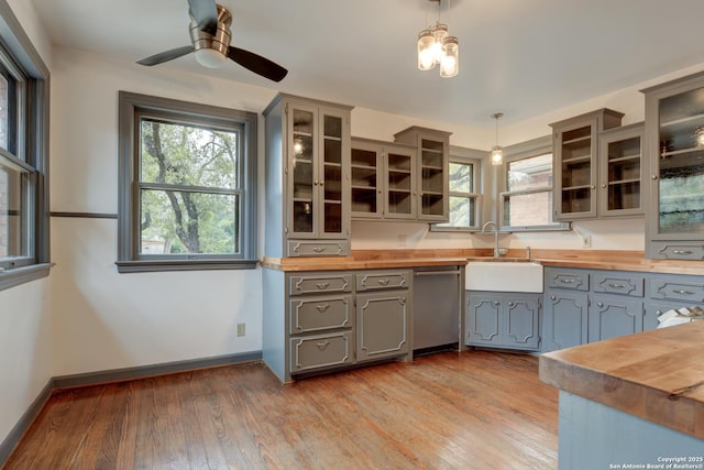 kitchen featuring butcher block counters, gray cabinetry, stainless steel dishwasher, sink, and pendant lighting