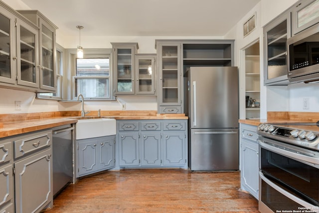 kitchen with gray cabinetry, sink, pendant lighting, stainless steel appliances, and butcher block countertops