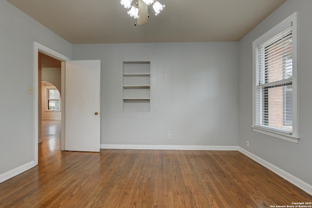 unfurnished room featuring built in shelves, a healthy amount of sunlight, and hardwood / wood-style flooring