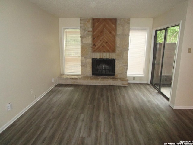 unfurnished living room with a textured ceiling, a stone fireplace, and dark wood-type flooring