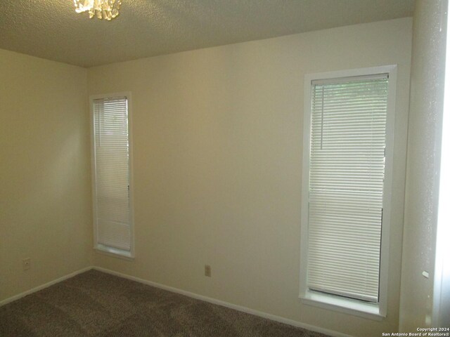 carpeted spare room featuring a chandelier and a textured ceiling