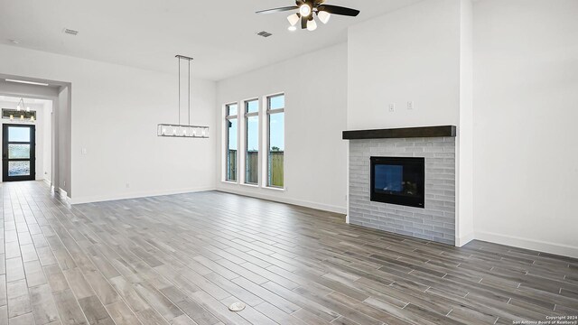 unfurnished living room featuring baseboards, ceiling fan with notable chandelier, wood finished floors, and a healthy amount of sunlight