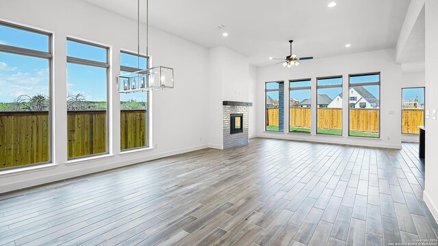 unfurnished living room with a stone fireplace, ceiling fan, and light hardwood / wood-style floors