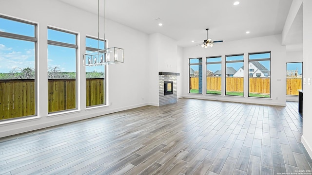 unfurnished living room featuring baseboards, recessed lighting, wood finished floors, and ceiling fan with notable chandelier