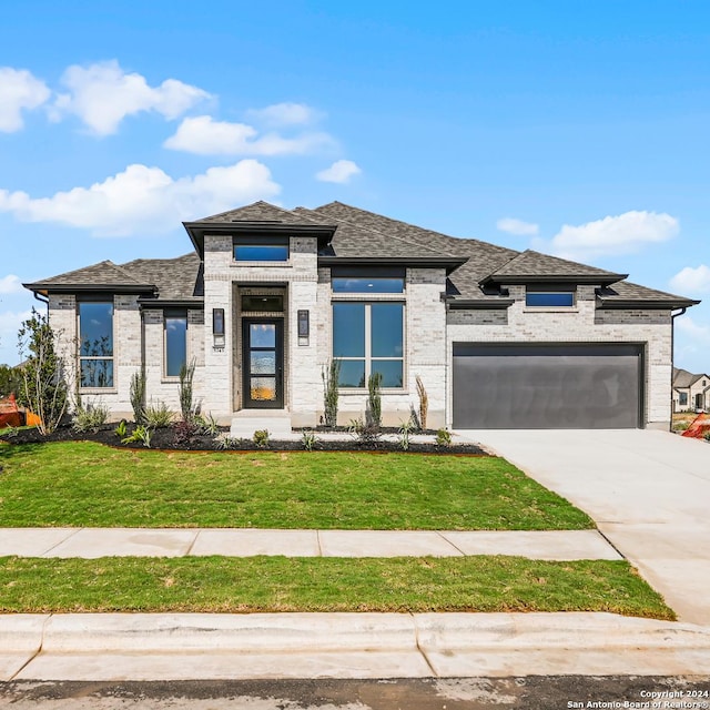 prairie-style home with driveway, a garage, a front lawn, and brick siding